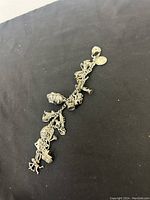 Full view of the sterling silver charm bracelet displaying multiple detailed charms against a black surface.