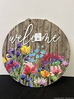 Full view of round welcome sign with floral pattern and text on wood plank background.