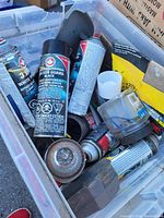 Photo showing plastic bin filled with various spray paint cans, paint caps, and other miscellaneous items.