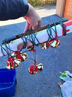 Photo showing a string of six gold metal Christmas bells decorated with red ribbons on green wire.