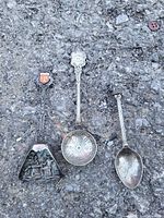 Photo showing three metal collector spoons placed on a grey textured surface.
