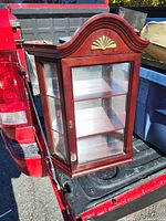 Front and side view of a wooden display case with curved top and glass panels, sitting in truck bed.