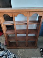 Photo showing entire wooden display shelf with three vertical sections and four shelves each, decorative arch cutouts at top, with light surface wear.