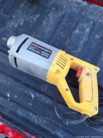 Electric concrete vibrator lying on a dark surface showing the side label and handle details.