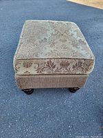 Front view of a rectangular foot stool with brown floral damask fabric on the cushion top and ribbed corduroy upholstery on the sides. The stool has four round wooden feet.