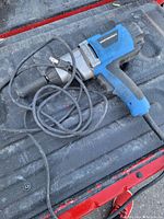 Full view of the blue and black Mastercraft impact wrench laying on a red and black surface, showing the cord and side handle.