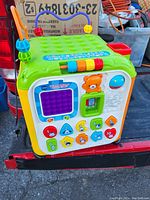 Colorful interactive educational kids toy cube with various buttons, shapes, a bead maze, and a small window with a bear figure inside shown from front angle.