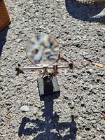 Magnifying glass on adjustable metal stand with alligator clips, placed on rough outdoor surface.