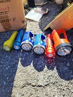 Five flashlights arranged in a row on asphalt, showing size and design differences.