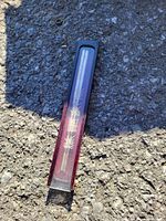 Photo shows a pair of metal chopsticks inside a transparent plastic case with a dark backing and Asian script on the case, on a rough textured surface.