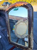 Photo of a rectangular mirror with an arched top and distressed wooden frame showing wear and aging.