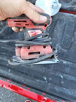 Close-up photo of a red Milwaukee electric palm sander held in hand showing the power cord wrapped around it and the sanding pad at the bottom.