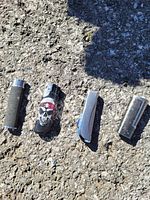 Four assorted lighters in sunlight on rough surface, showing different designs and materials.