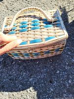 Closed wicker sewing kit case with woven handle and blue accents on woven pattern.