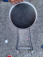 Top view of the round folding stool showing the black seat with signs of use and the silver metal frame.