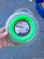 Photo of round neon green trimmer line coiled in clear plastic packaging with label showing diameter and brand