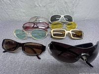 8 pairs of sunglasses arranged on a grey surface showing variety of frame and lens colors and styles