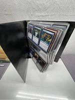 Open black binder with multiple plastic sleeves filled with Magic: The Gathering cards shown from an angle to display the quantity and condition of cards.
