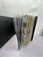 Side view of a black binder filled with plastic sleeves holding dozens of Pokémon cards.