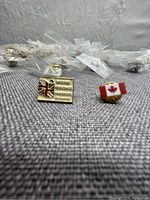 Close-up photo showing one British flag pin with Union Jack and text, and one Canada flag pin with red maple leaf.