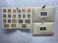 Photo showing two official DAPOSTA 1937 envelopes with attached stamps and a half sheet of used postal stamps pinned on album pages.