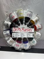 Circular plastic holder with 12 arranged small squeeze bottles of watercolor paint showing product labels and colors.