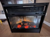 Front view of electric fireplace showing glowing embers and flame effect inside glass panel, unit turned on.