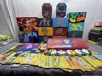 Front view of collection showing stacked themed Pokémon storage boxes including Elite Trainer Boxes, tins, plush toys, Poké Ball containers, and a large assortment of Pokémon cards spread out.