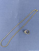 Gold plated fine chain necklace and gold tone floral cluster ring on blue background.