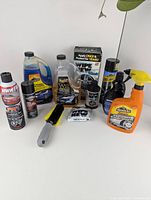 Front view of assortment of auto detailing and cleaning products including bottles, cans, spray bottles, and applicator brush.