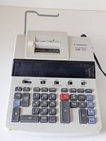 Front view of Canon CP1200DII printing calculator showing keyboard, numeric keys, and printing mechanism on top.