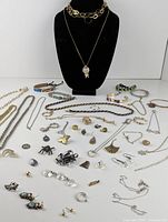Wide view of mixed costume jewelry pieces including necklaces, bracelets, rings, earrings, pendants spread on white surface with a black display bust in center.