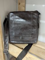 Full front view of dark brown leather messenger bag with flap and adjustable shoulder strap.