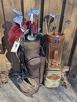 Two golf bags with multiple golf clubs positioned outdoors on a wooden background.