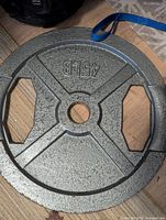 Single 45lb gray cast iron Olympic weight plate placed on wood floor, showing front side with '45LB' embossed and cutout handles