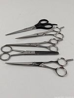 Five hair scissors laid flat showing variety of handle styles, sizes, and one thinning shear with toothed blade.
