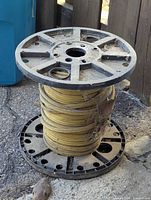 Photo of the yellow heavy duty electrical wire wound on a black plastic spool outdoors, showing surface dirt and debris on the spool.