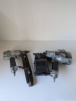 Two Hitachi pneumatic nailers shown from above on a white surface: a coil nailer on left and a finish nailer on right.