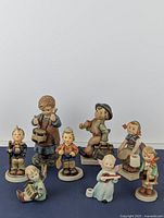 Full view of all nine Hummel figurines arranged on flat surface showing various poses and characters including musical and everyday props.