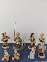 Full lot overview showing nine Hummel Goebel figurines arranged on blue surface against white background
