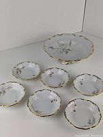 All seven bowls arranged on a table including one large serving bowl and six smaller bowls showing butterfly and floral detail with gold trim.