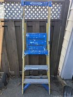 Front view of the Werner folding step ladder showing the fiberglass yellow side rails and blue metal platform and steps with paint marks.