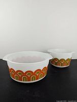 Two white glass Pyrex casserole dishes with orange and olive green arch pattern shown side by side