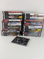 Photo displaying 34 PS2 game cases stacked in two piles with an additional open case showing disc.