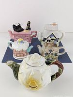 Overview of all 5 decorative ceramic teapots displayed on a dark surface, showing shapes and colors.