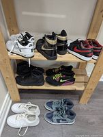 Top shelf with three pairs of Nike sneakers: white Air Force 1 low-top, black and gold Air Jordan high-top, and black and red Air Jordan low-top.