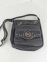 Front view of black leather Michael Kors shoulder bag showing flap pocket with MK logo and studs, and top zippered pocket.
