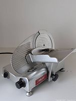 Front view of silver aluminum meat slicer showing blade, carriage, thickness knob and brand label.