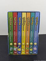 Side view of all seven Pokémon Adventures graphic novels in a box set showing colorful spines with volume numbers and Pokémon images.