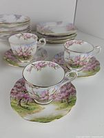 Side view of three floral teacups on matching saucers with gold trim and scenic blossom design.